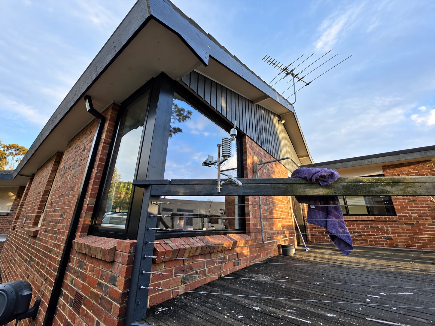Black corner glazing beneath a gable roof, viewed upward from a timber deck
