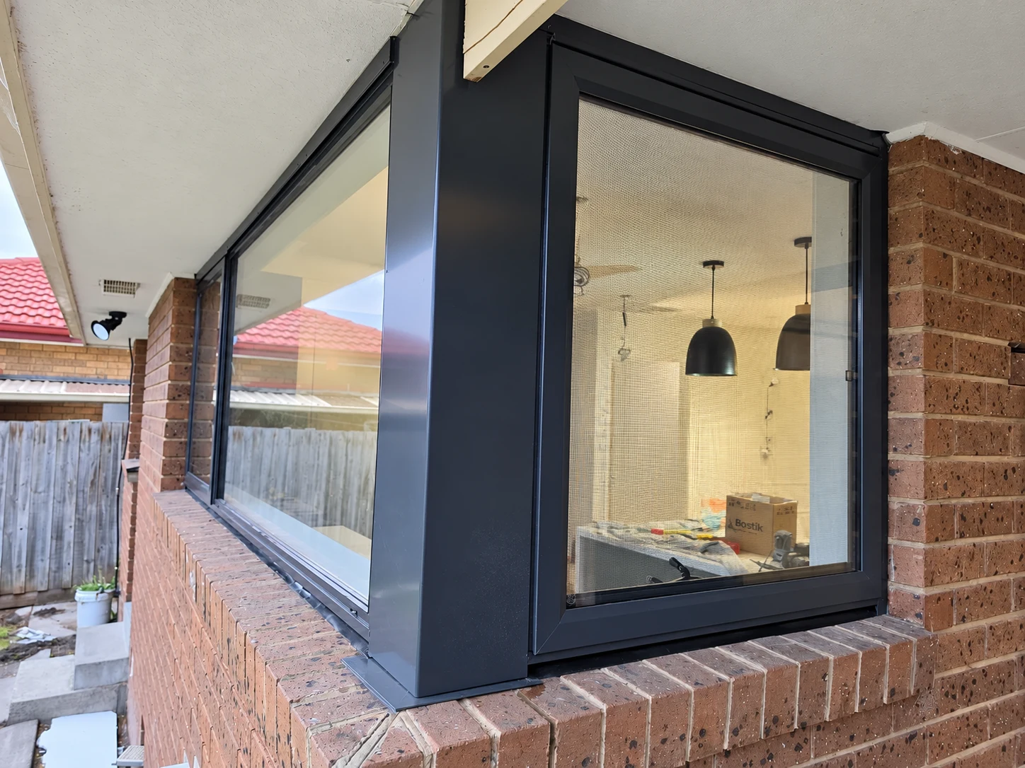 Detailed exterior view of a black aluminium corner window and brick sill with pendant lights inside
