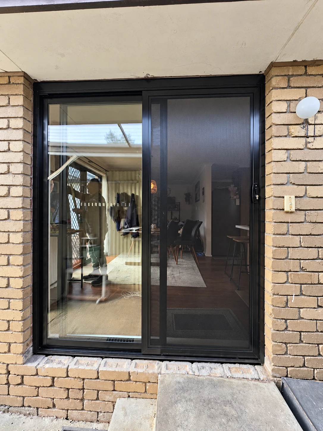 Black framed glass door with a sliding screen between cream brick walls