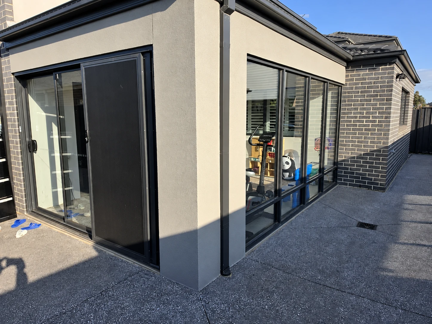 Black aluminium glass doors and large windows around the corner of a rendered and dark brick extension