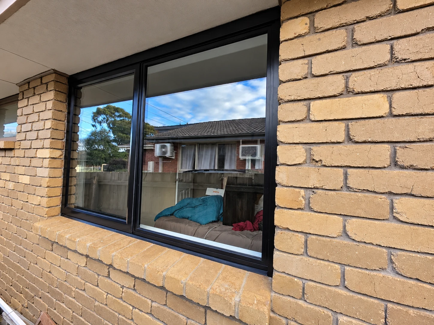 Black aluminium window and brick sill viewed along the outside of a cream brick home