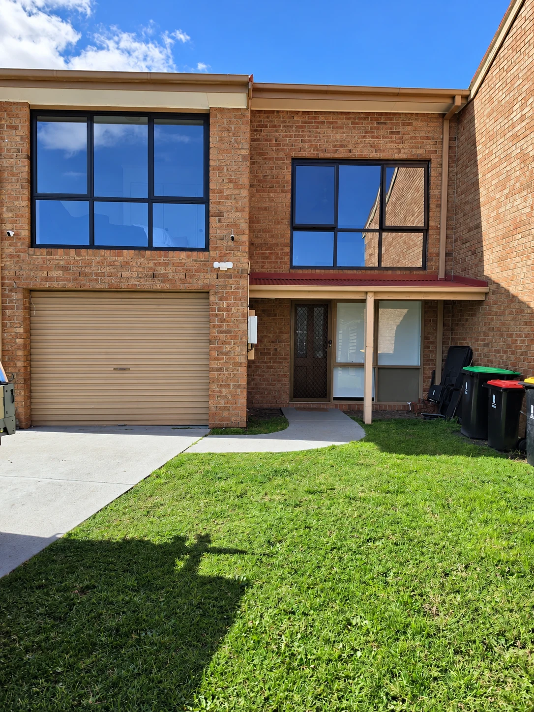 Brick townhouse facade with large black aluminium window frames above a garage and entrance