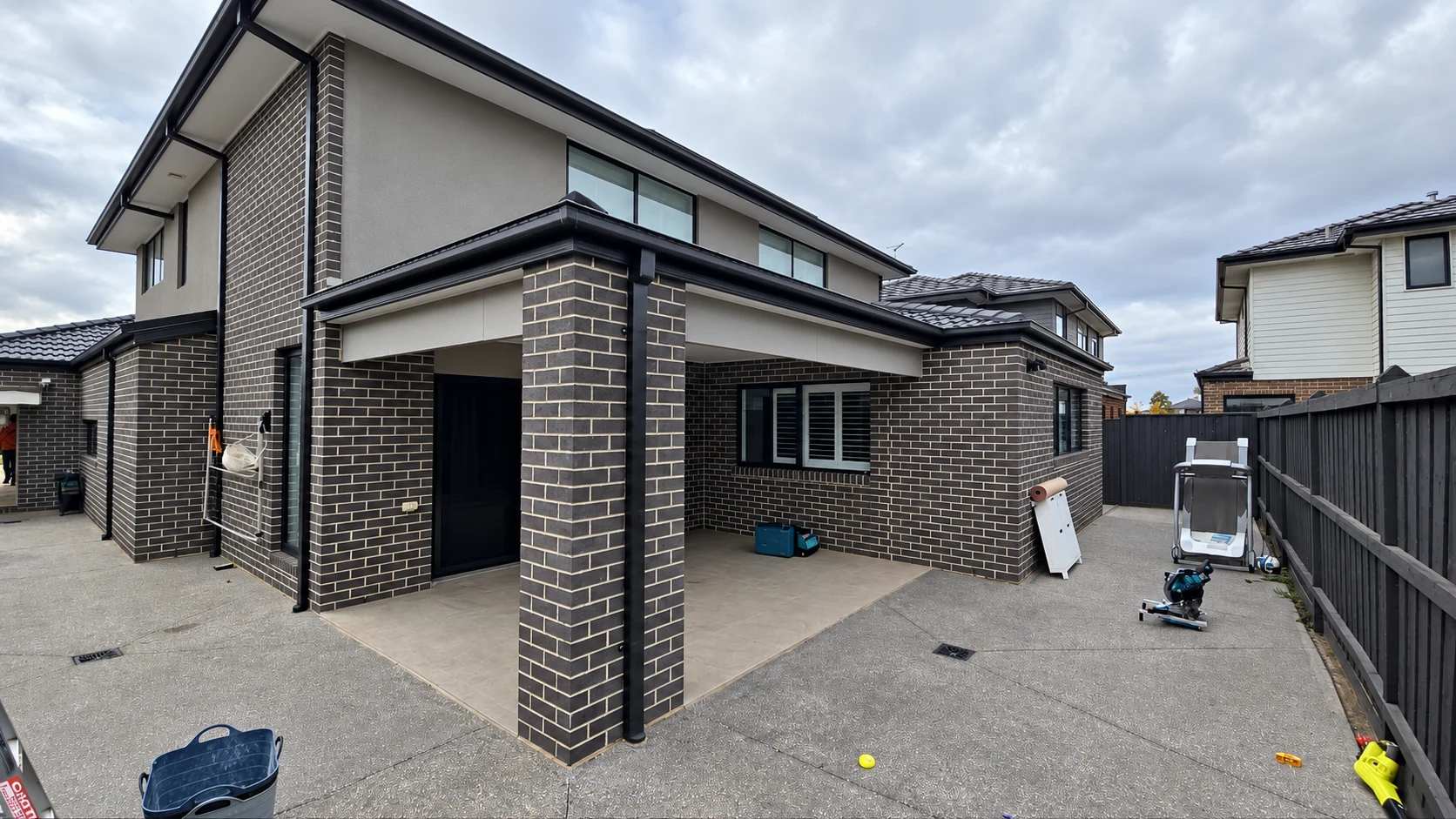 Contemporary two-storey extension with dark brickwork, black framed glazing and installation equipment outside