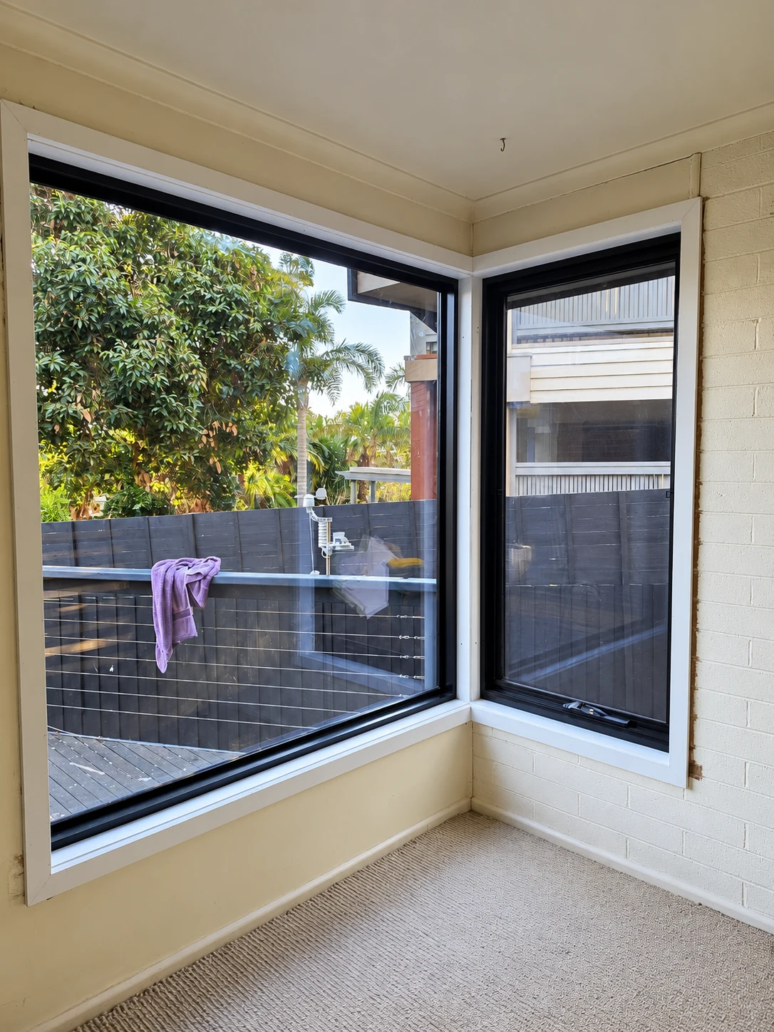 Interior corner with black aluminium windows, cream walls and a timber deck outside