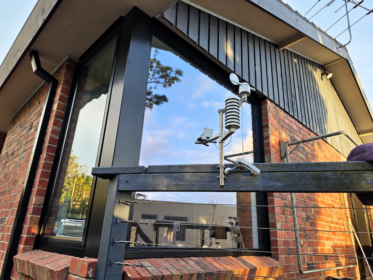 Low angle view of black corner glazing, red brickwork, dark cladding and a timber deck railing