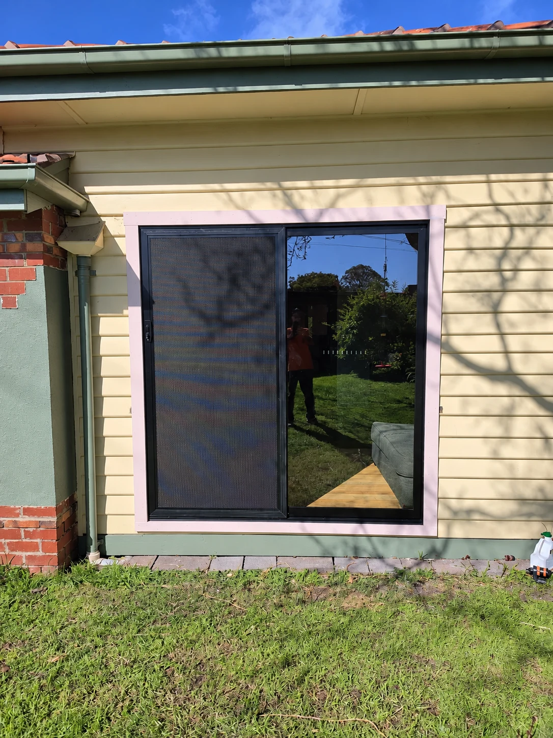 Dark framed window with a mesh screen set into a pale weatherboard wall