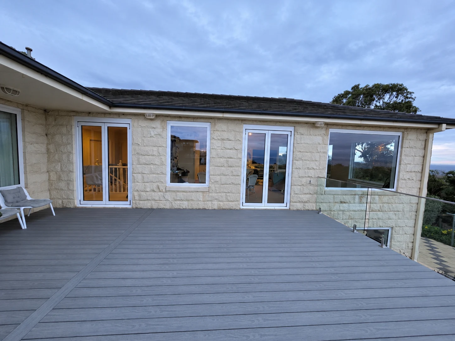 White framed windows and glazed doors opening onto a broad grey timber deck