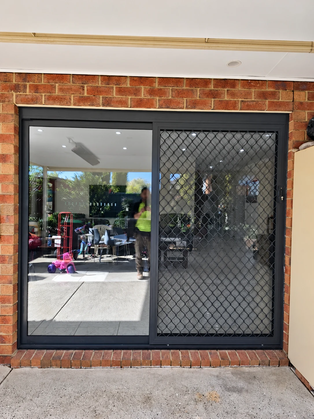 Dark framed glass door and diamond mesh security screen fitted into a brick opening