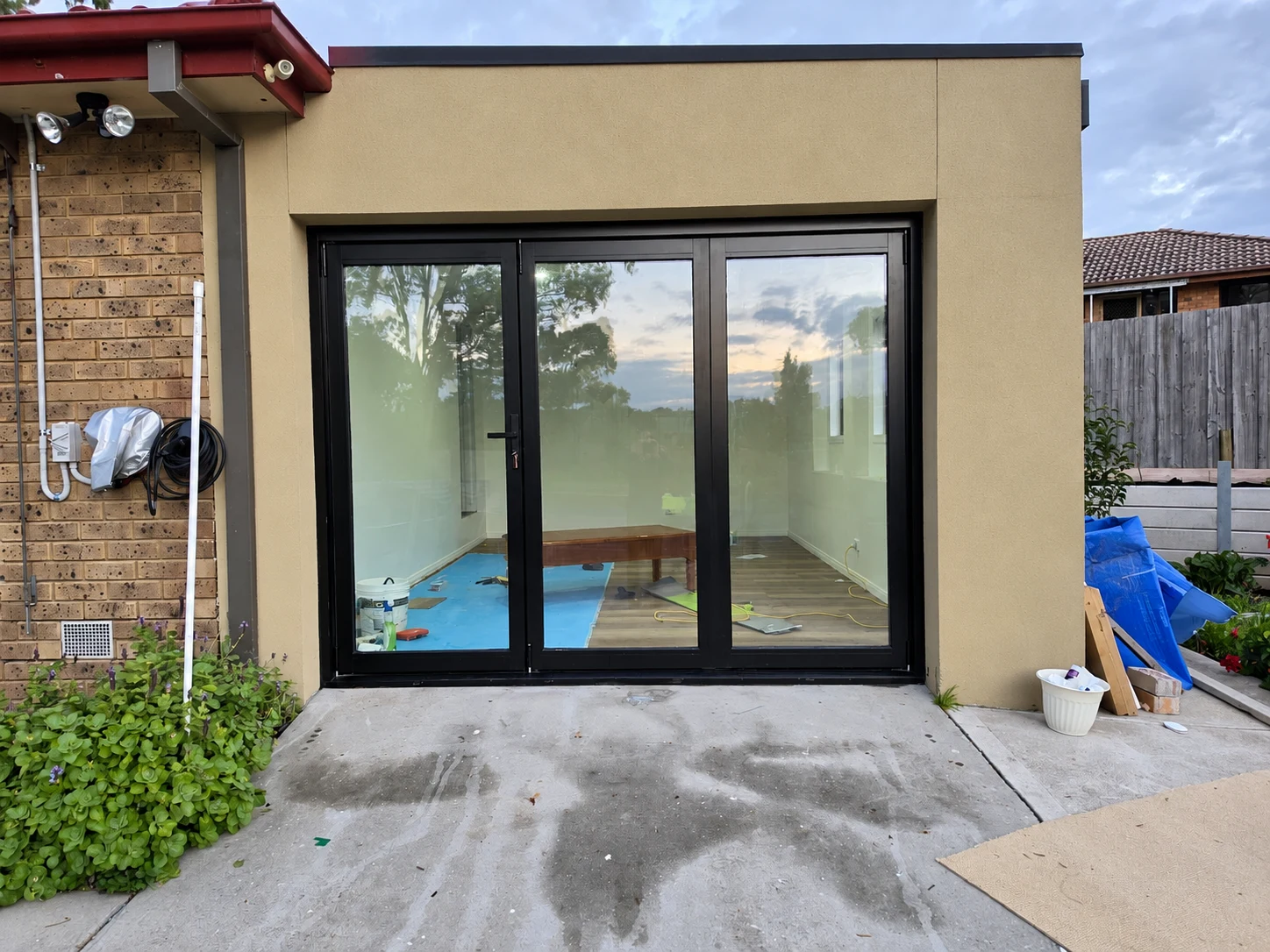 Three-panel black framed glass door within a rendered extension during finishing work
