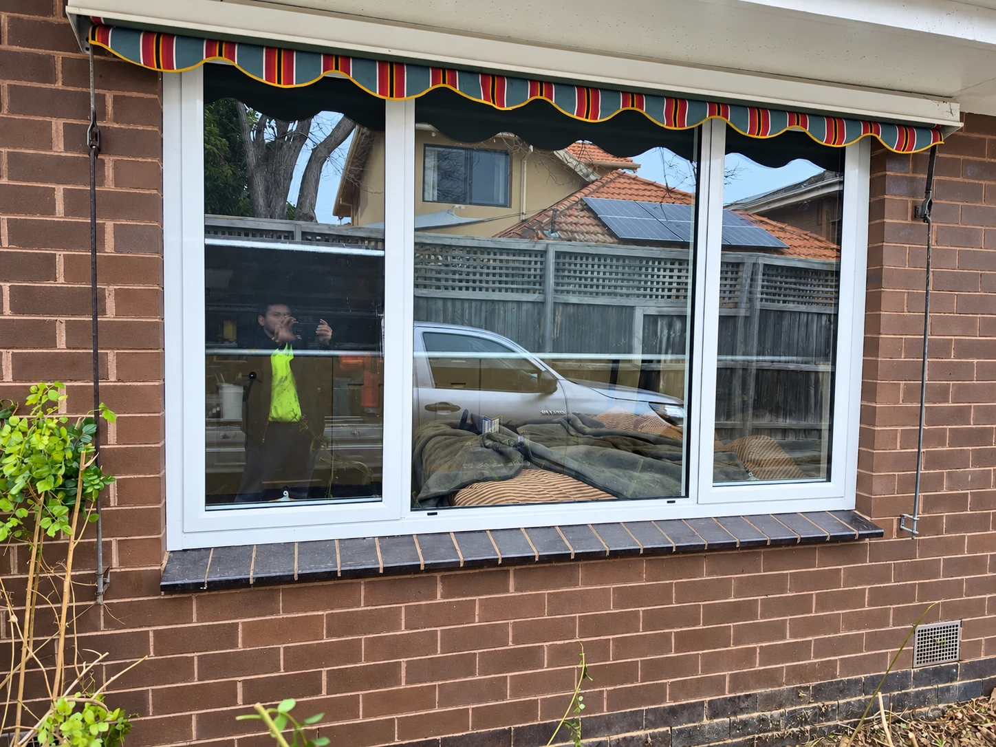 White aluminium window with three glazed sections beneath a striped outdoor awning