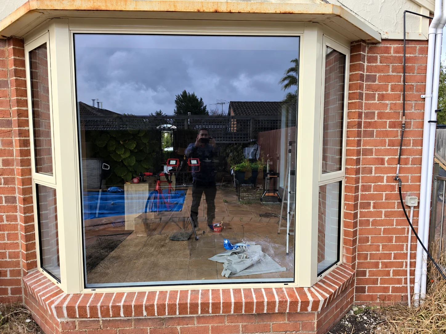 White framed bay window in red brickwork with garden reflections in the glass