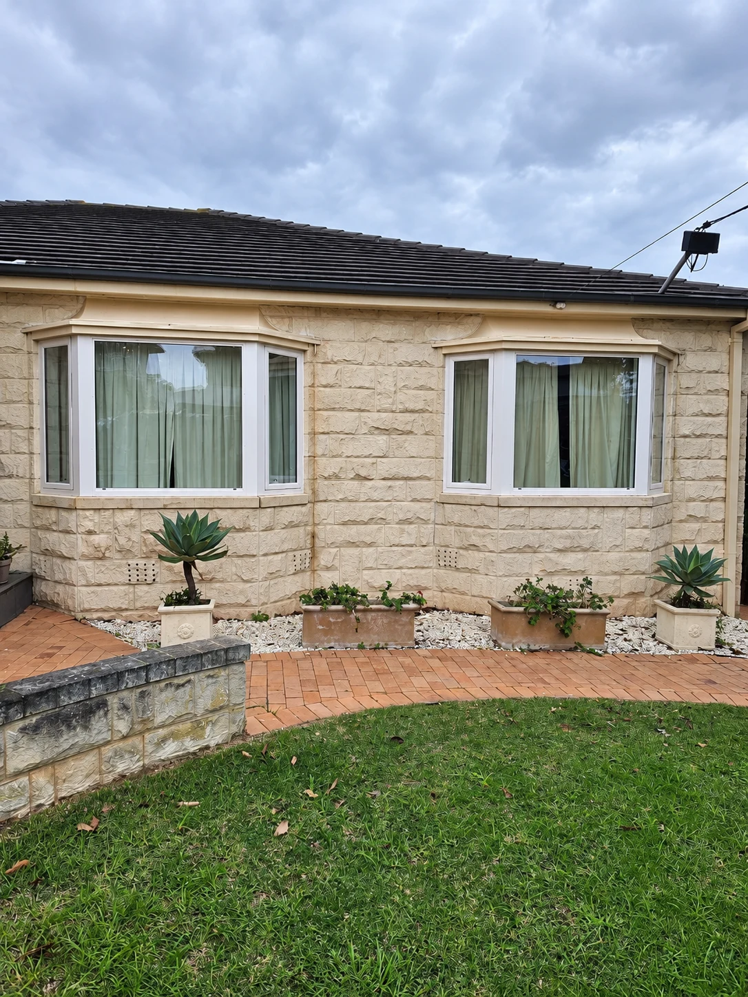 Stone house facade with white bay windows, garden planters and a brick path