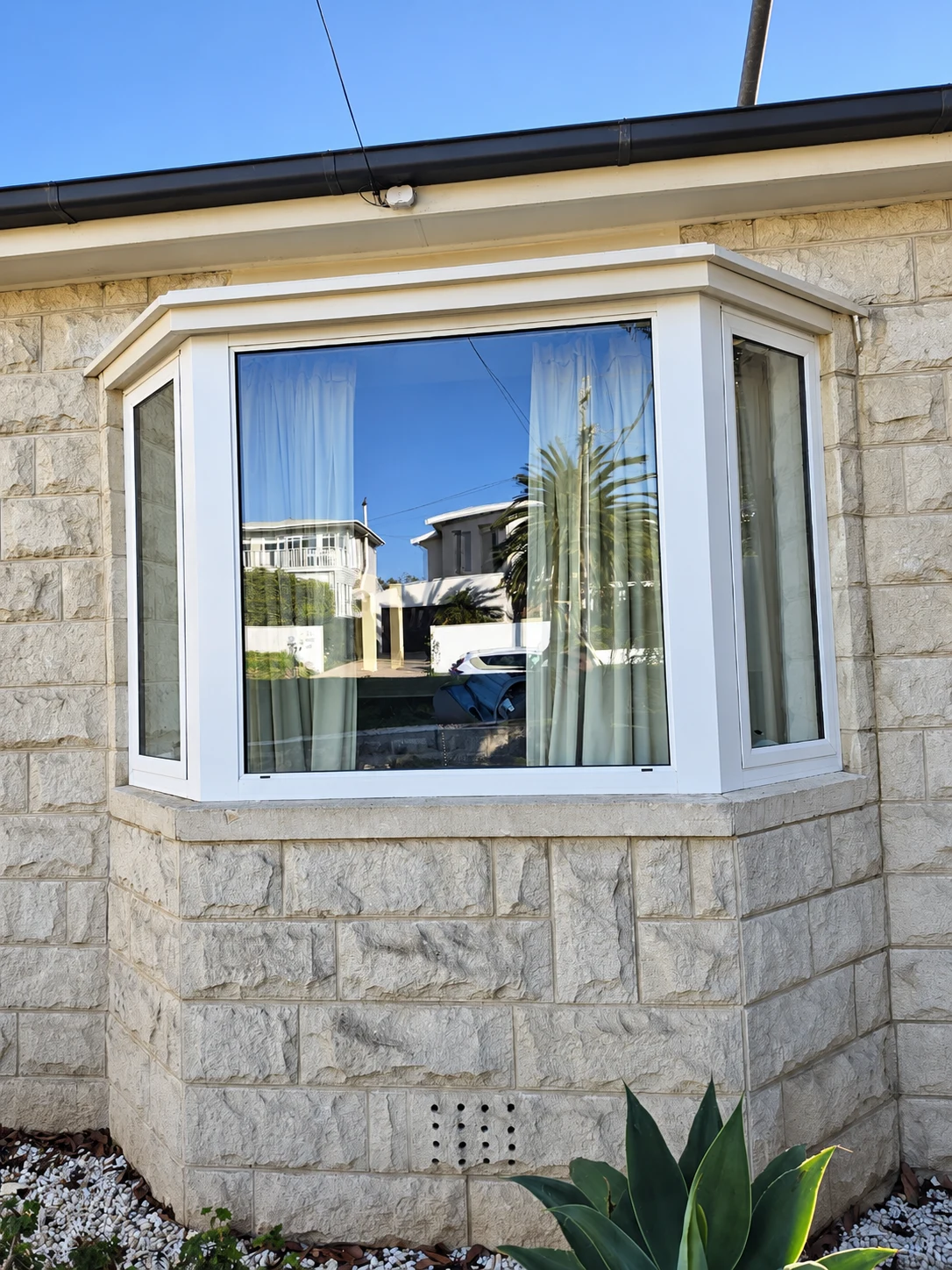 White framed bay window set into a pale stone facade with garden planting below