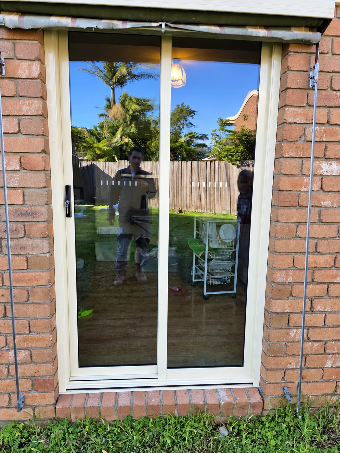 White framed two-panel glass door in a brick wall reflecting a garden and palm tree