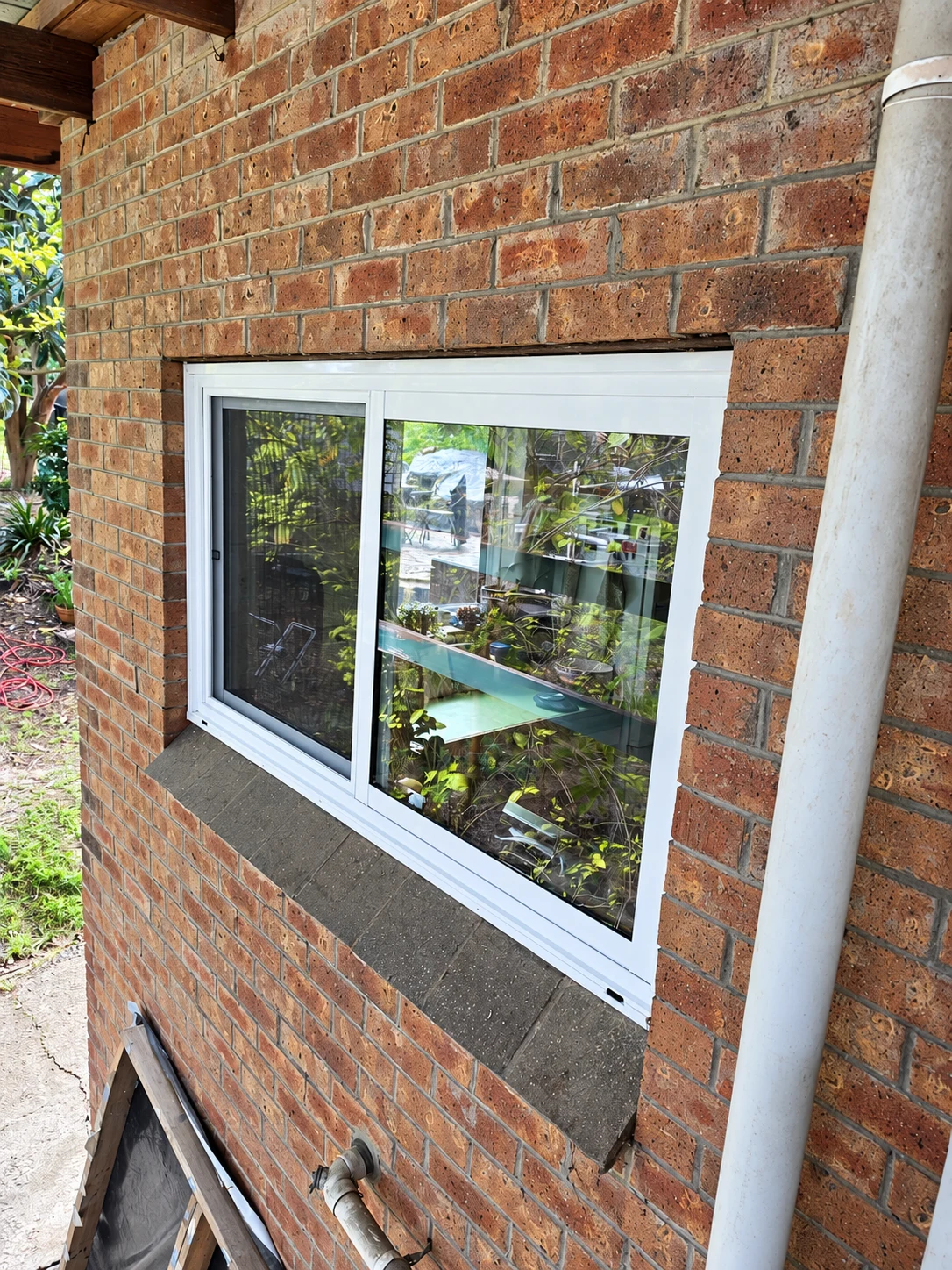 White aluminium sliding window fitted into a brick wall beneath a timber verandah